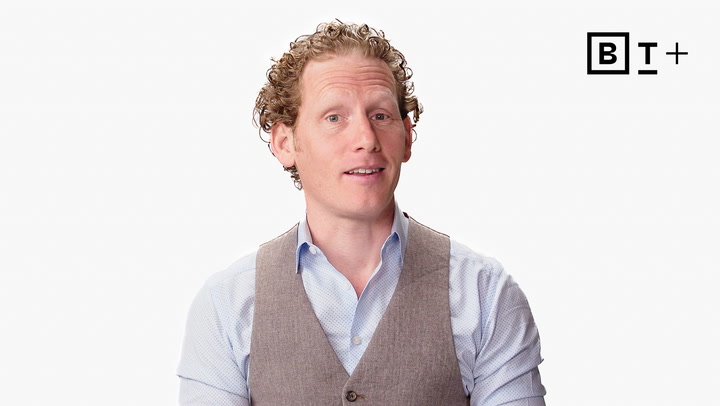 A man with curly hair wearing a light blue shirt and beige vest stands in front of a white background with the "BT+" logo in the top right corner.