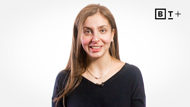A woman with long brown hair, wearing a black top and a necklace, smiles at the camera. A black and white "BT+" logo is visible in the top right corner.