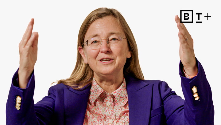 A person wearing glasses and a purple blazer gestures with both hands raised, palms facing each other, against a plain background with a "B T +" logo.