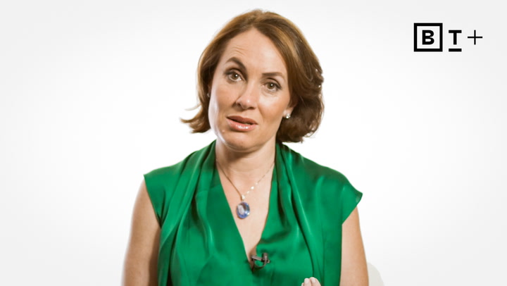 A woman with short brown hair wearing a green blouse and a pendant necklace speaks in front of a white background with a "B T +" logo in the corner.