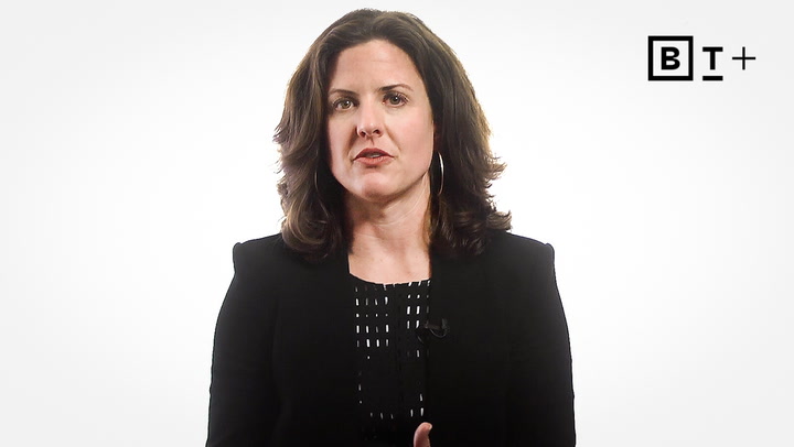 Woman with medium-length brown hair wearing a black blazer and patterned top, speaking against a plain white background with a "BT+" logo in the top right corner.