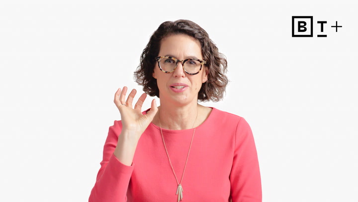 A woman in glasses and a pink top gestures with her right hand. There is a black "B T +" logo in the top right corner on a plain white background.