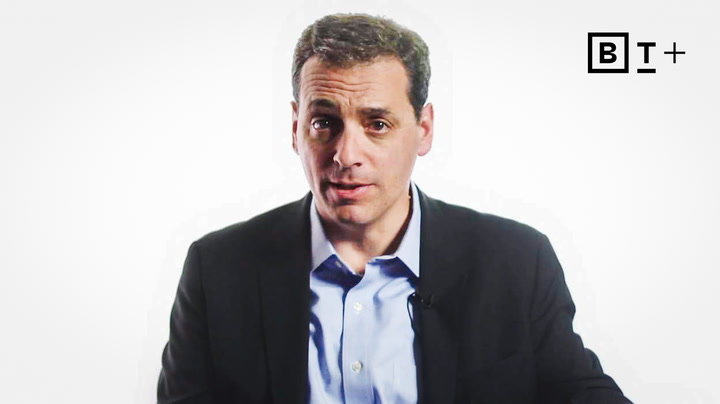 A man in a suit jacket and blue shirt faces the camera against a white background, with the B+ logo in the top right corner.