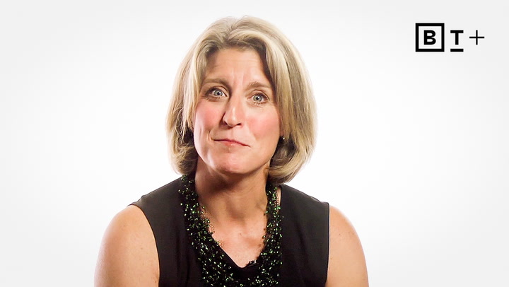 A woman with short blonde hair wearing a sleeveless black top sits in front of a plain white background with a "B T+" logo in the top right corner.
