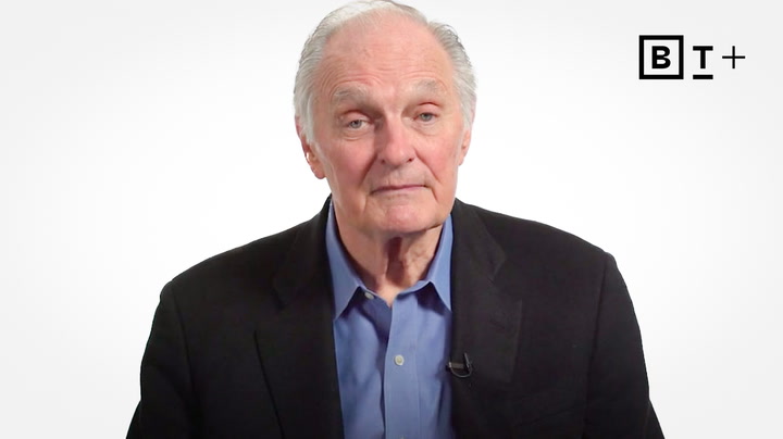 Older man in a dark blazer and blue shirt sits against a plain white background with a rectangular "BT+" logo in the upper right corner.