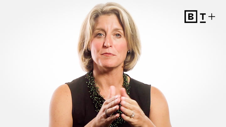 A woman with short blonde hair, wearing a black sleeveless top and beaded necklace, gestures with her hands against a plain white background. "B T +" logo appears in the top right corner.