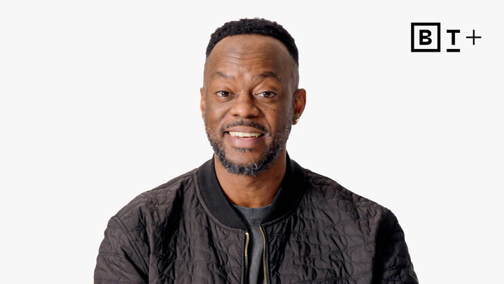 A man with a short beard and mustache smiles at the camera, wearing a black quilted jacket. The background is white with a "B T +" logo in the top right corner.