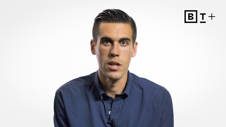 A man in a blue button-up shirt sits facing the camera against a plain white background with a "BT+" logo in the top right corner.