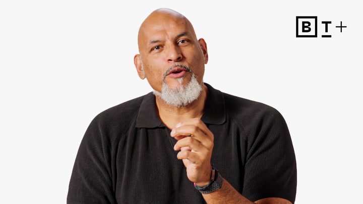 A bald man with a gray goatee, wearing a black shirt, speaks while gesturing with his right hand. The BT+ logo is visible in the top right corner.