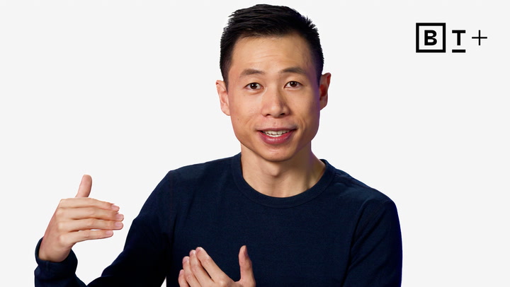 A man in a navy blue shirt gestures with his hands while speaking. The B+ logo appears in the top right corner against a plain white background.