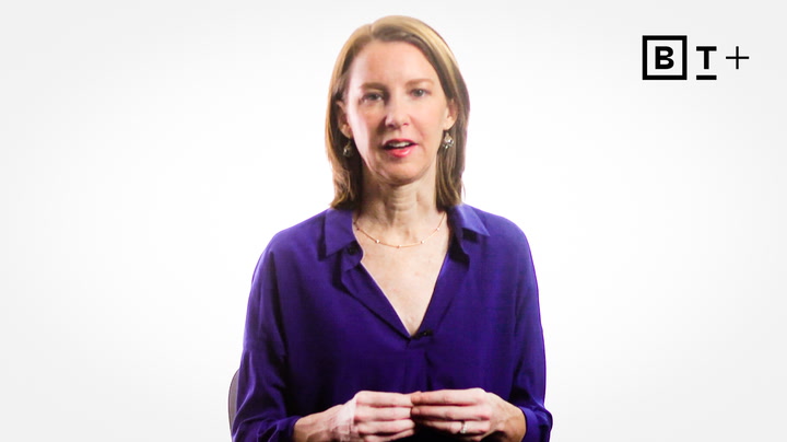 A woman with straight, shoulder-length brown hair wears a purple blouse and stands in front of a plain white background with a "BT+" logo in the top right corner.