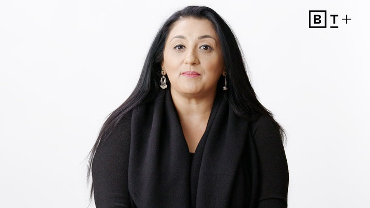 A woman with long black hair, wearing a black top and earrings, is facing the camera against a plain white background with a "BT+" logo in the top right corner.