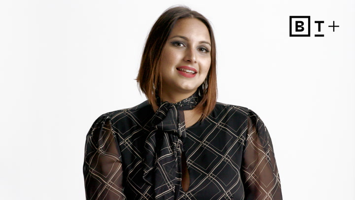 A person with shoulder-length hair in a patterned black blouse poses against a white background with a "BT+" logo in the top right corner.