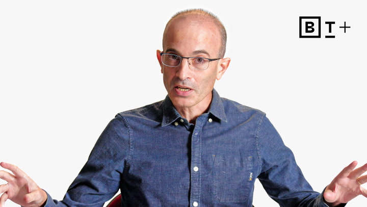 A man with glasses and a blue button-up shirt speaks while gesturing with his hands; a "B T +" logo appears in the top right corner.
