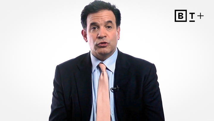 A man in a suit and tie sits in front of a white background with the B T plus logo in the top right corner.