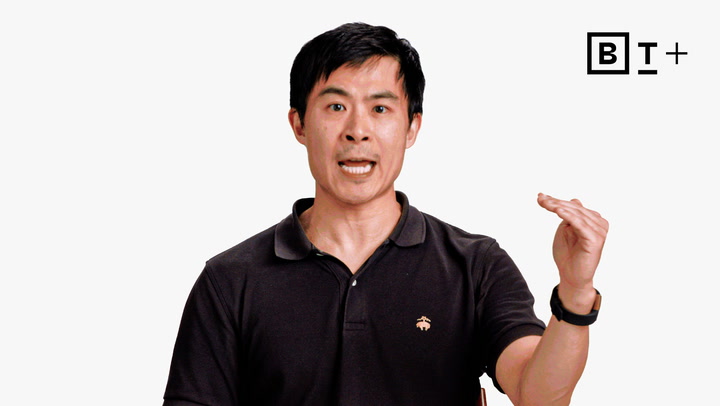 A man in a black polo shirt speaks while gesturing with his right hand raised; a "B T +" logo appears in the top right corner.