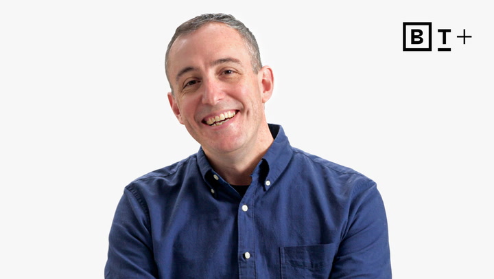 A man wearing a blue button-up shirt smiles at the camera against a plain white background. The "BT+" logo is visible in the top right corner.
