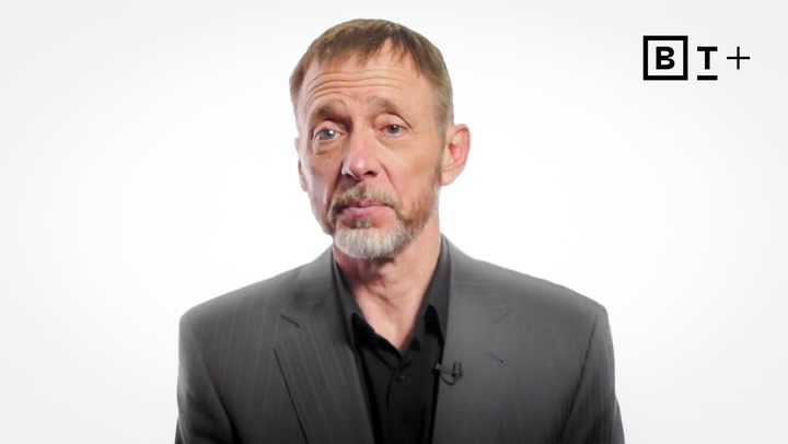 A man with short hair, a trimmed beard, and a gray suit looks at the camera against a plain white background with a "BT+" logo in the top right corner.