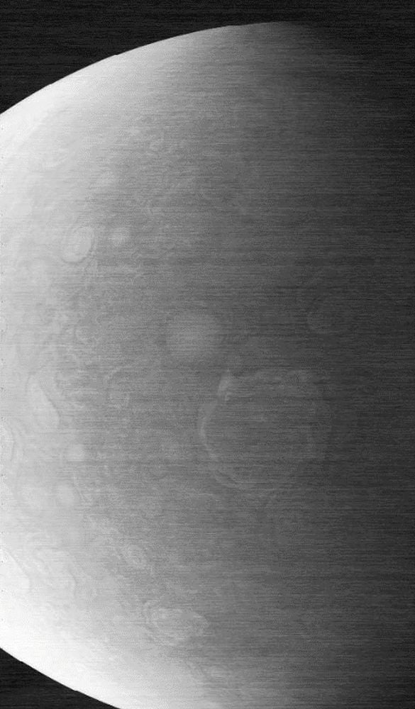 Grayscale image showing a partially shadowed, cloud-covered planet with visible atmospheric patterns, likely taken from space during the NASA Juno mission.
