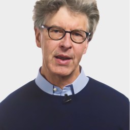 An older man with gray hair and glasses wearing a navy sweater over a light blue collared shirt, speaking in front of a plain white background.
