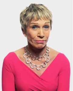 A woman with short blonde hair wears a bright pink top and a chunky silver necklace, looking at the camera with a neutral expression against a plain background.
