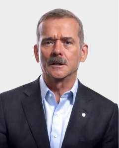 A middle-aged man with short hair and a mustache, wearing a dark blazer and light blue shirt, poses against a plain light background.