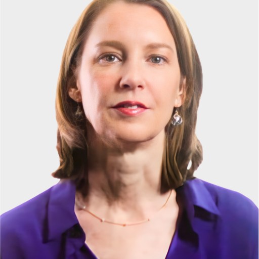 A woman with shoulder-length brown hair, wearing a purple blouse, drop earrings, and a delicate necklace, poses against a plain light background.
