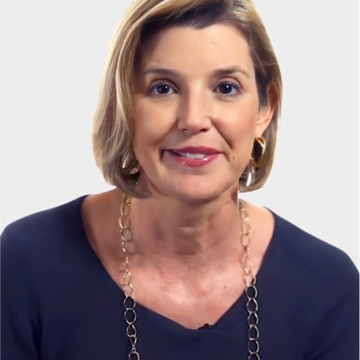 A woman with short blonde hair, wearing a dark top and a long chain necklace, is looking at the camera against a plain background.