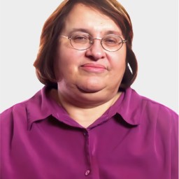 A middle-aged woman with short brown hair, glasses, and a purple button-up shirt is looking at the camera against a plain light background.