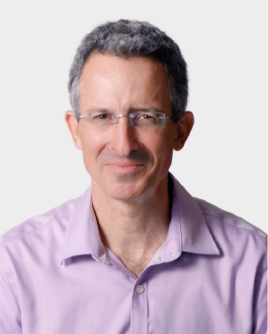 A middle-aged man with short, gray hair and glasses, wearing a light purple collared shirt, is smiling at the camera against a plain background.