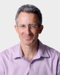 A middle-aged man with short, gray hair and glasses, wearing a light purple collared shirt, is smiling at the camera against a plain background.