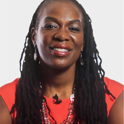 A woman with long braided hair, wearing a red top, earrings, and a beaded necklace, is smiling at the camera against a plain white background.
