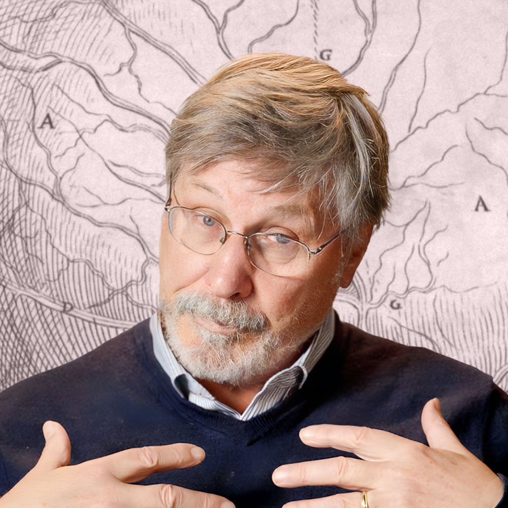 An older man with gray hair, glasses, and a beard gestures towards himself, standing in front of a background featuring a black and white anatomical diagram.
