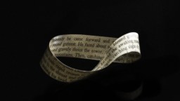 A Möbius strip made from paper with printed text is displayed against a dark background.