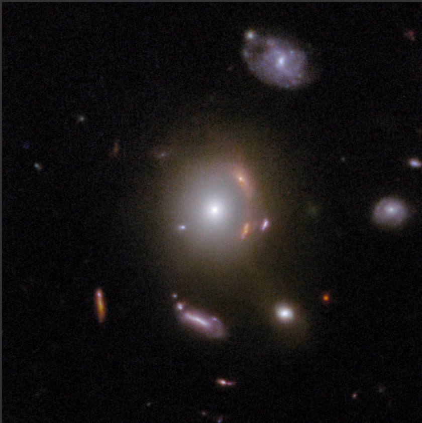 A bright elliptical galaxy, captured by COSMOS-Web JWST, is surrounded by gravitational lens arcs and smaller galaxies against a dark space background filled with faint stars and distant objects.