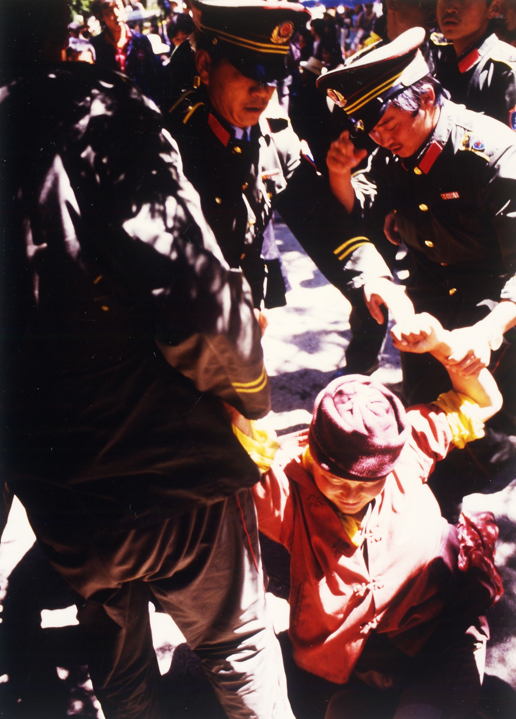 Three uniformed officers in China are detaining and lifting a person in red clothing who is seated on the ground.